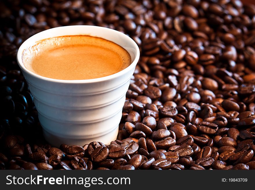 A close-up image of coffee beans with a cup of expresso