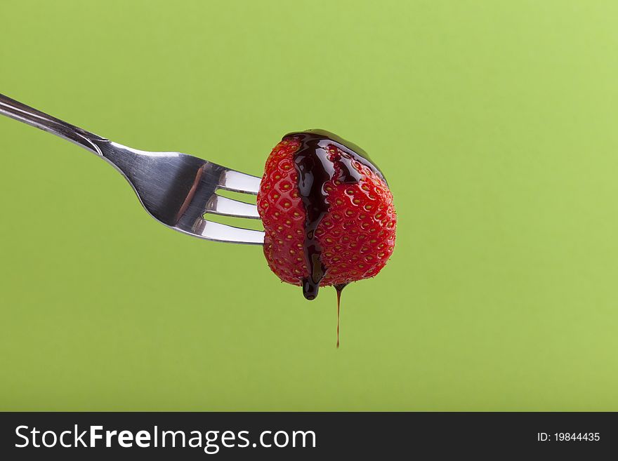 Studio-shot of a fork with a strawberry with dripping chocolate syrup on a green background. Studio-shot of a fork with a strawberry with dripping chocolate syrup on a green background.