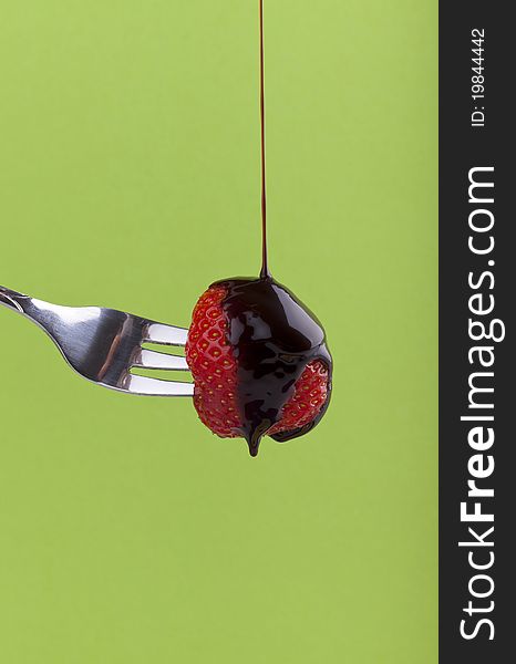 Studio-shot of a fork with a strawberry with dripping chocolate syrup on a green background. Studio-shot of a fork with a strawberry with dripping chocolate syrup on a green background.