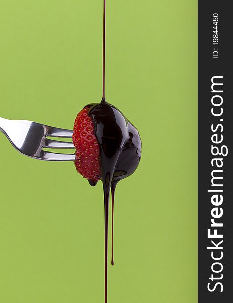 Studio-shot of a fork with a strawberry with dripping chocolate syrup on a green background. Studio-shot of a fork with a strawberry with dripping chocolate syrup on a green background.