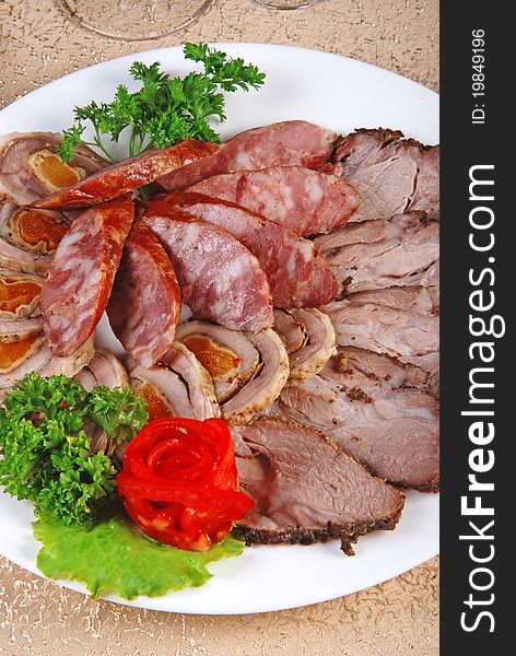 Meat and sausages with parsley and vegetables on white plate. Closeup. Meat and sausages with parsley and vegetables on white plate. Closeup