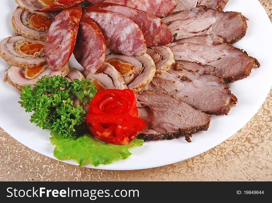 Meat and sausages with parsley and vegetables on white plate. Closeup. Meat and sausages with parsley and vegetables on white plate. Closeup