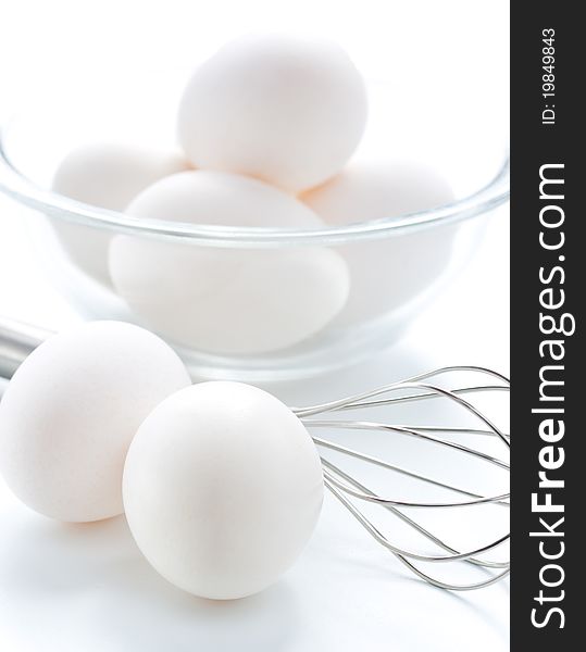 Metal whisk and fresh eggs in bowl, over white background.