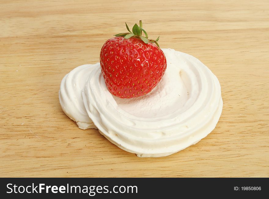 Single ripe strawberry in a meringue nest on a wooden food preparation board. Single ripe strawberry in a meringue nest on a wooden food preparation board