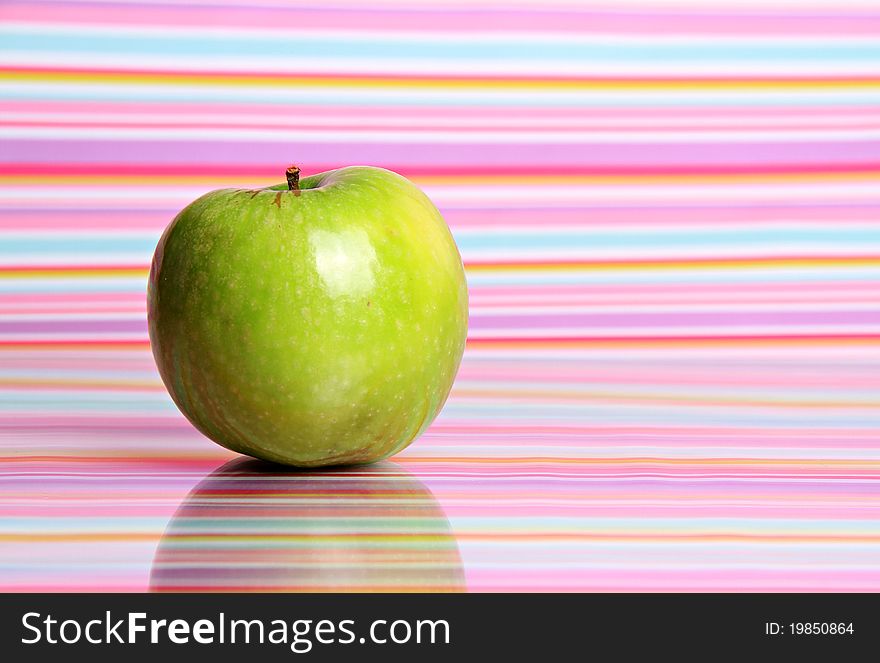 A bright green apple sits alone against a reflective stripy background. A bright green apple sits alone against a reflective stripy background