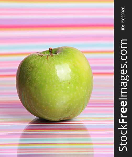 A bright green apple sits alone against a reflective stripy background. A bright green apple sits alone against a reflective stripy background