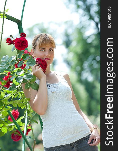 Young pretty woman holding and smelling red rose in park. Young pretty woman holding and smelling red rose in park