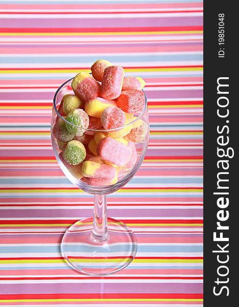 A large glass full of multi coloured tasty sugary sweets against a coloured stripy background. A large glass full of multi coloured tasty sugary sweets against a coloured stripy background.