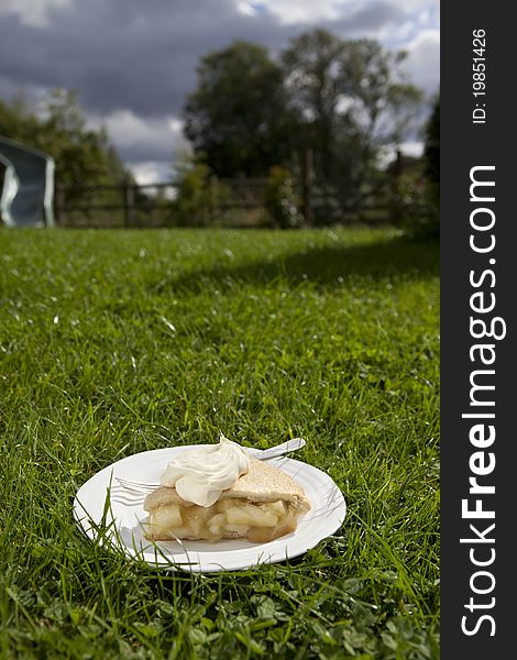 Apple pie and cream served on a plate and placed on a garden lawn