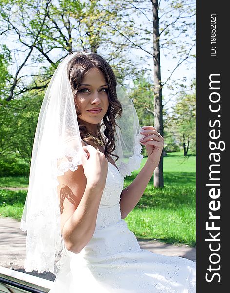 Beautiful young bride sitting on a park bench