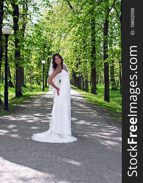 Young bride standing in an alley in the park at summer day