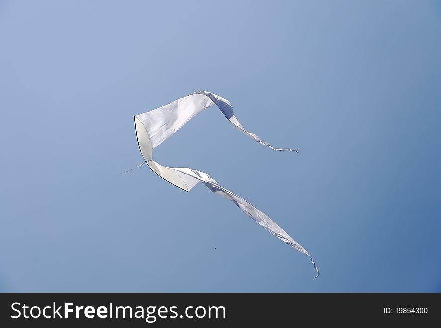 White kite soaring against blue sky. Summer Kite Festival