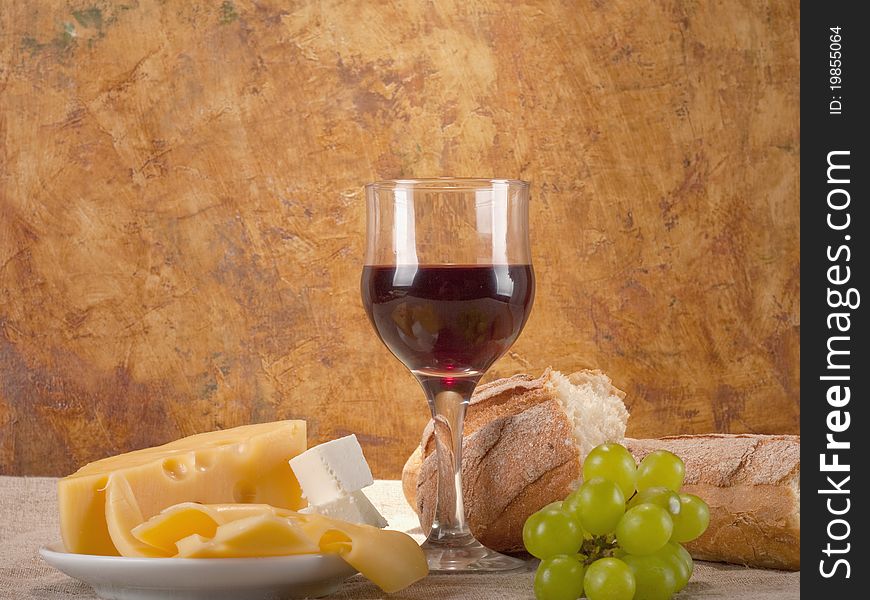 Red wine, assorted cheeses, bread and grapes in a still life setup.