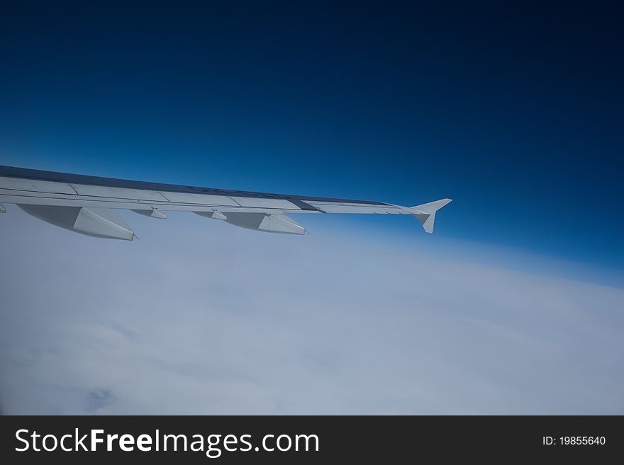 View of an airplane wing above the clouds and against blue sky from the inside of an aircraft