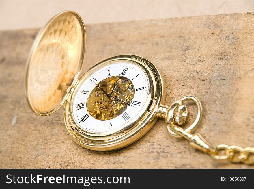 The golden pocket watch on the rough wood board. The golden pocket watch on the rough wood board