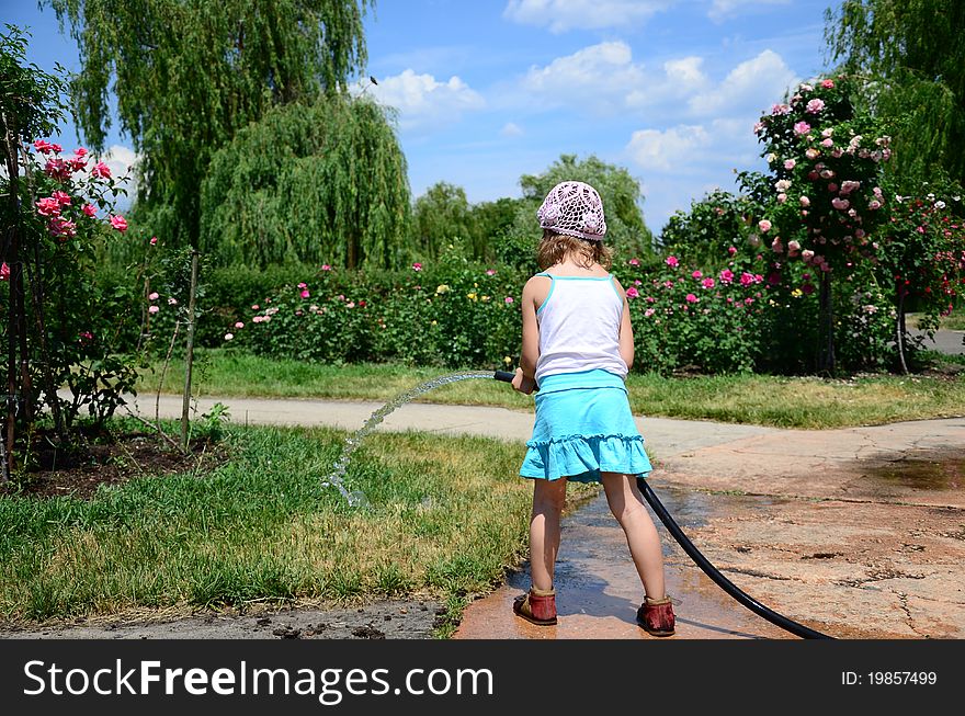 Little girl with a hose watering the flowers