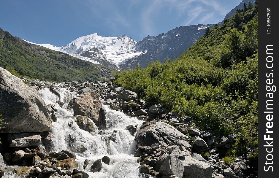 View of high mountains with snow and rapid stream.