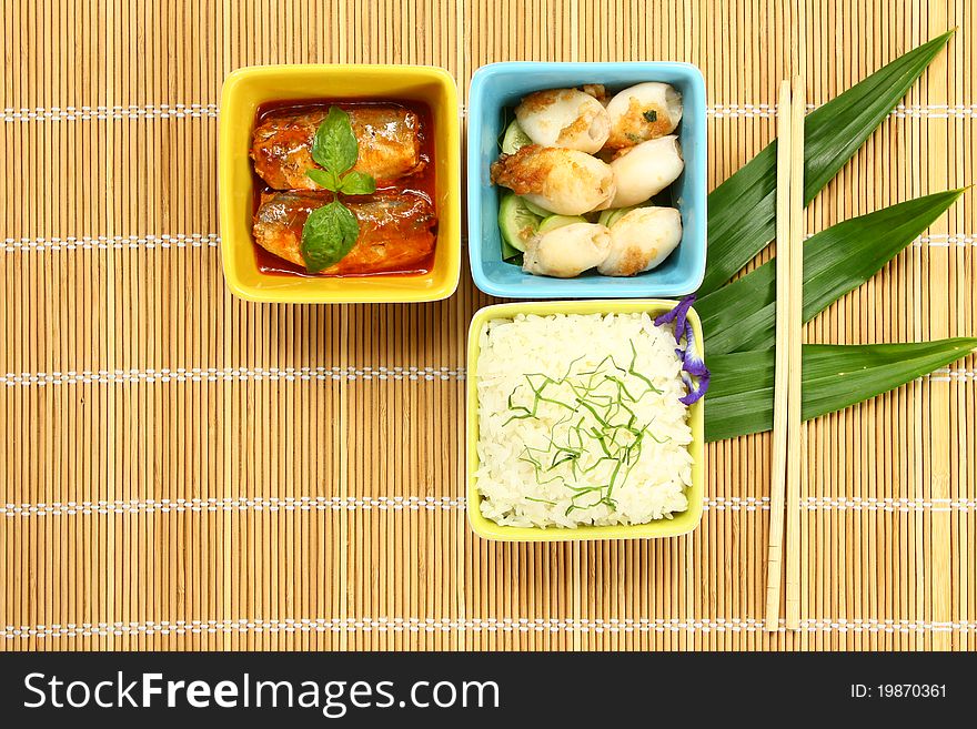 Cooked rice with fish in sauces and fried cuttlefish on bamboo pad. Cooked rice with fish in sauces and fried cuttlefish on bamboo pad