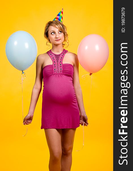 Lovely pregnant young woman with balloons over yellow background