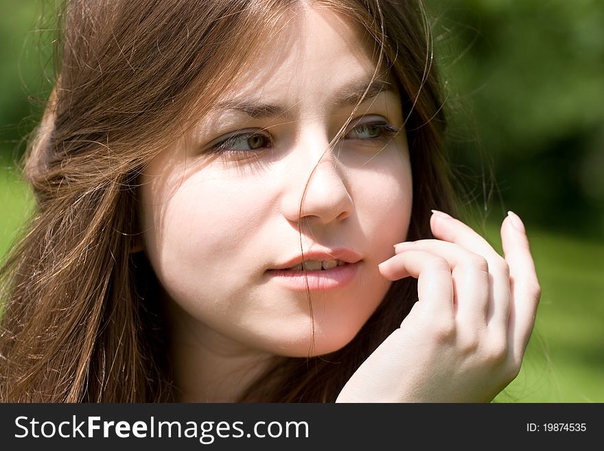 Portrait of young woman with clear skin is touching her face by hand in park on green background. Portrait of young woman with clear skin is touching her face by hand in park on green background