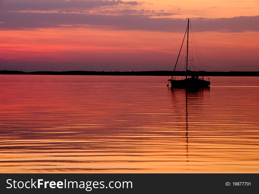 Silhouette of a sailboat on a calm golden lake at sunset. Silhouette of a sailboat on a calm golden lake at sunset