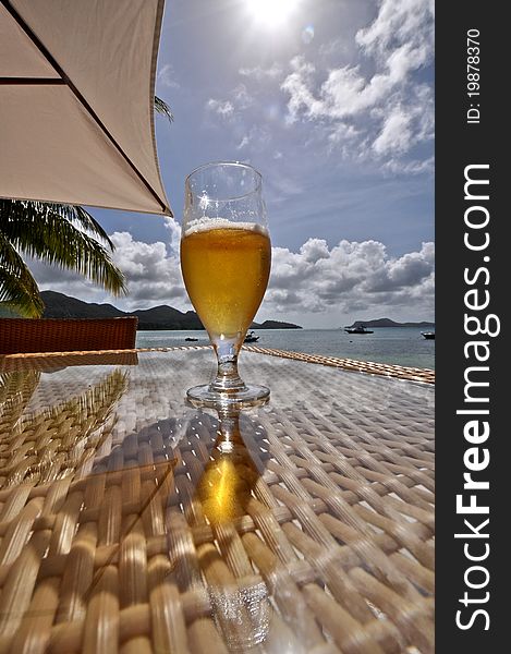 Sun lit glass of beer on beach table