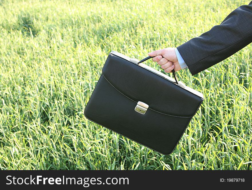 Hand businessman with briefcase against the backdrop of the field. Hand businessman with briefcase against the backdrop of the field