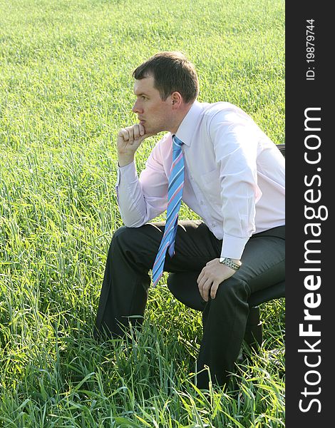 Pensive businessman sitting on meadow. Pensive businessman sitting on meadow