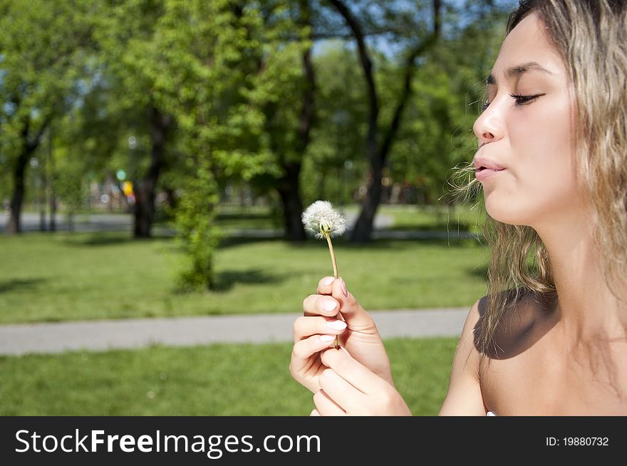 Young girl blowing on the dandelion in park