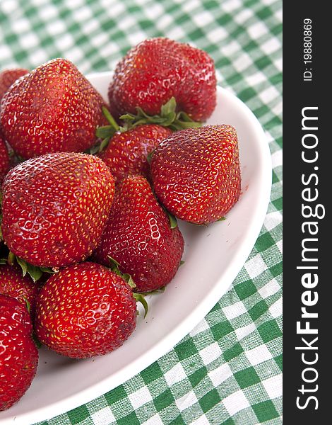 A lot of big ripe strawberries on a white plate, is on the table with green cloth. A lot of big ripe strawberries on a white plate, is on the table with green cloth