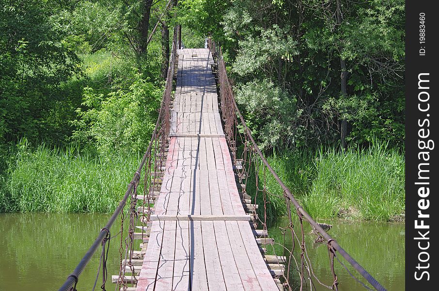 Old suspension walk bridge across river in forest