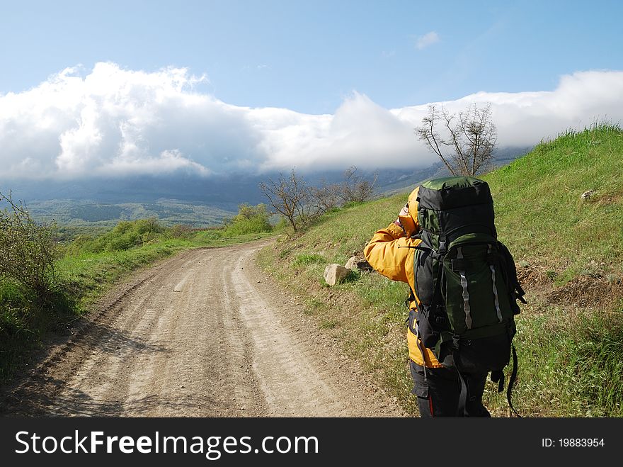 Hiker is shooting a landscape by video camera. He is standing on the natural road. He is carrying a large rucksack. Hiker is shooting a landscape by video camera. He is standing on the natural road. He is carrying a large rucksack.