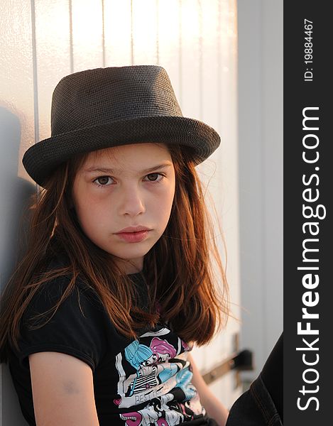 Young girl posing against a white beach cabin while wearing a black hat. Young girl posing against a white beach cabin while wearing a black hat