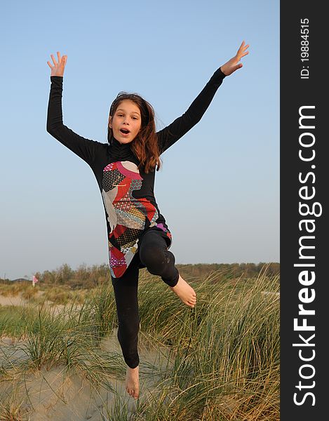 Young girl jumping for joy in the dunes at the beach