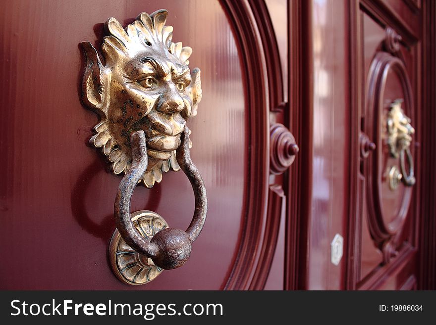 Close-up of a traditional Maltese door with gargoyle knockers in gold and red paint. Close-up of a traditional Maltese door with gargoyle knockers in gold and red paint.