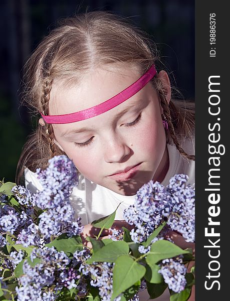 The young girl with a fair hair With a lilac bouquet against a dark background. The young girl with a fair hair With a lilac bouquet against a dark background