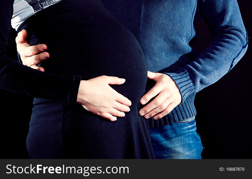 Pregnant woman and her husband caressing her belly with dark background