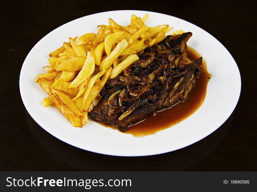 Steak and fries on a white plate, black background