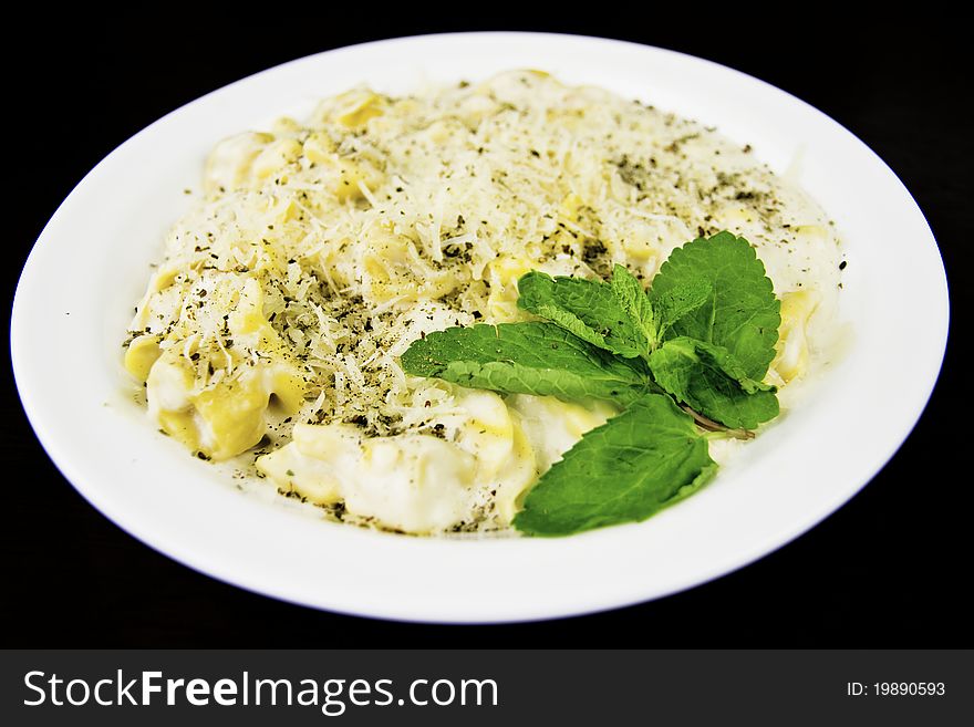 Tortellini with spices on a white plate, black background