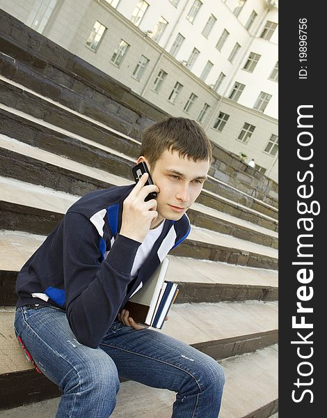 Close-up of a modern student talking on a cell phone on campus. In the hand holding books. Close-up of a modern student talking on a cell phone on campus. In the hand holding books