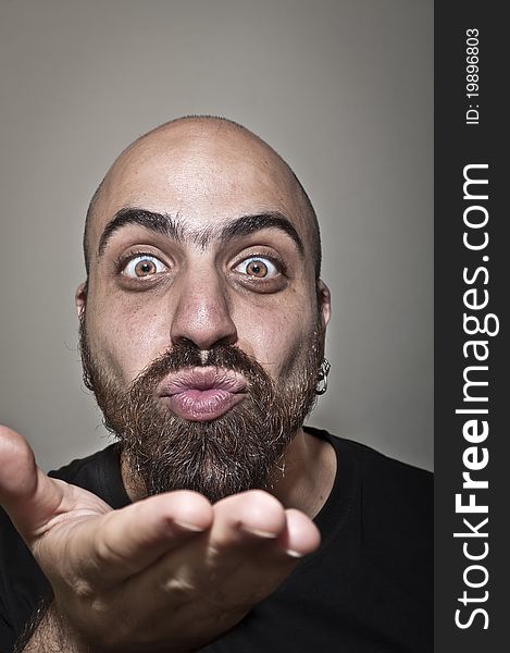 Man with a bushy beard that blows a kiss on grey background