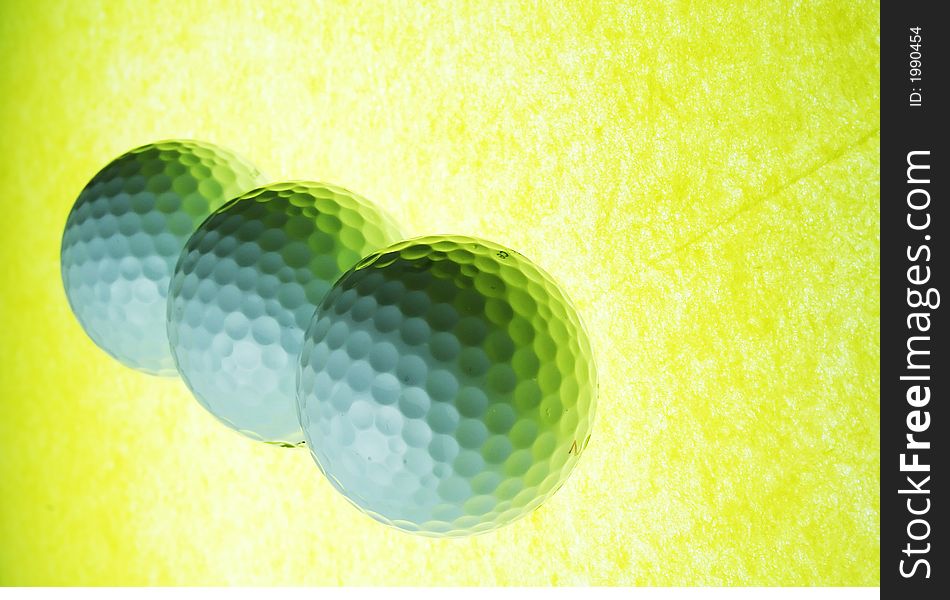 A trio of golf balls on yellow illuminated glass. A trio of golf balls on yellow illuminated glass