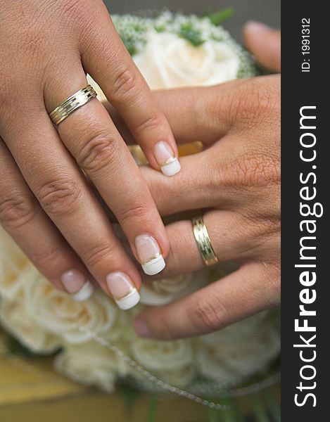The hands of newly married couple with wedding rings and roses in background