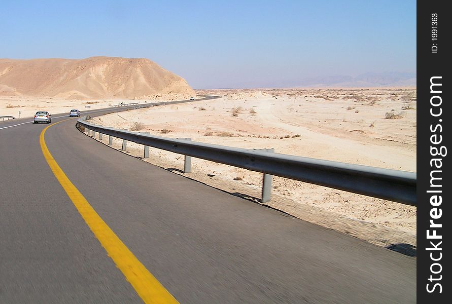 Asphalt road with two cars in Negev desert. Blue sky and desert around. Asphalt road with two cars in Negev desert. Blue sky and desert around