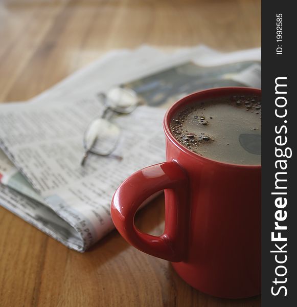 A cup of coffee, a newspaper and a pair of glasses, on a wooden table. A cup of coffee, a newspaper and a pair of glasses, on a wooden table