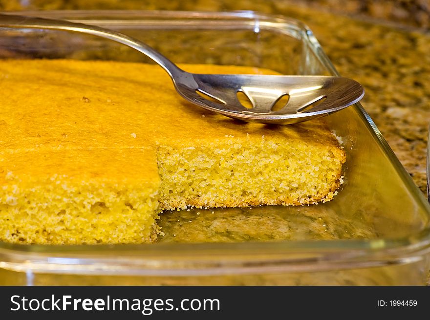 Fresh-baked, homemade, golden cornbread, still hot out of the oven with a silver serving spoon ready for use. Looks like someone has already sampled the cornbread!. Fresh-baked, homemade, golden cornbread, still hot out of the oven with a silver serving spoon ready for use. Looks like someone has already sampled the cornbread!