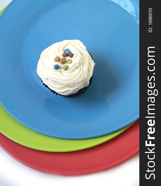 Three Ices cucpcake on a blue plate with coloured plates underneath. Three Ices cucpcake on a blue plate with coloured plates underneath