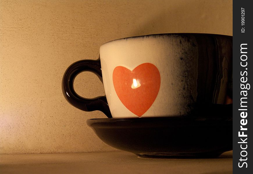 Teacup with a heart with the reflection of a burning candle. Teacup with a heart with the reflection of a burning candle.
