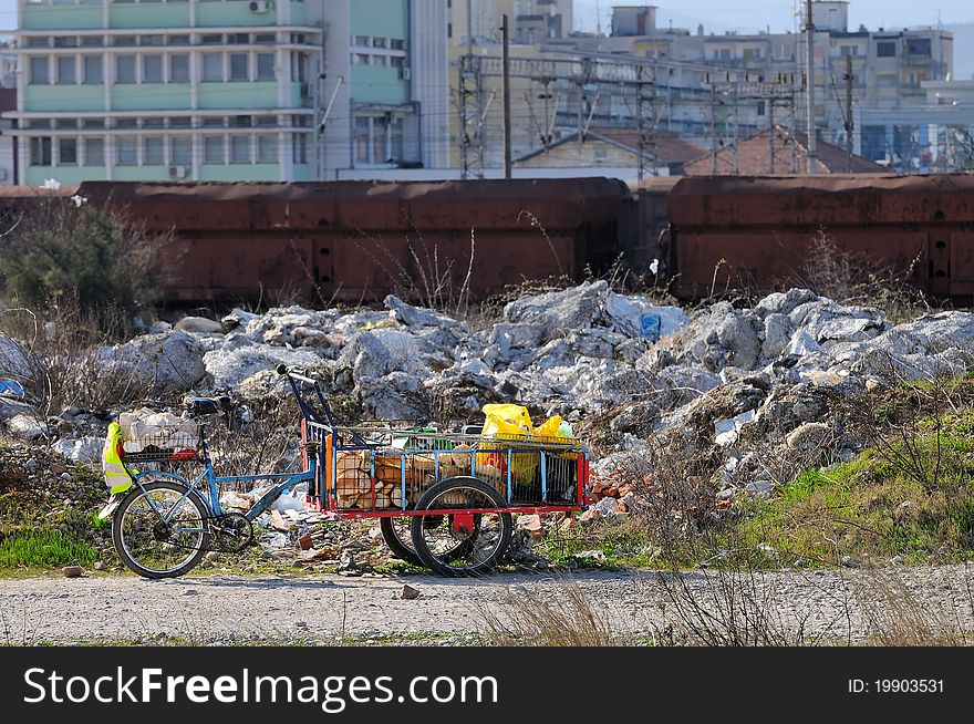 Bicycle on 3 wheels of a homeless individual full with food. Dirt, old train and buildings in the background. Bicycle on 3 wheels of a homeless individual full with food. Dirt, old train and buildings in the background