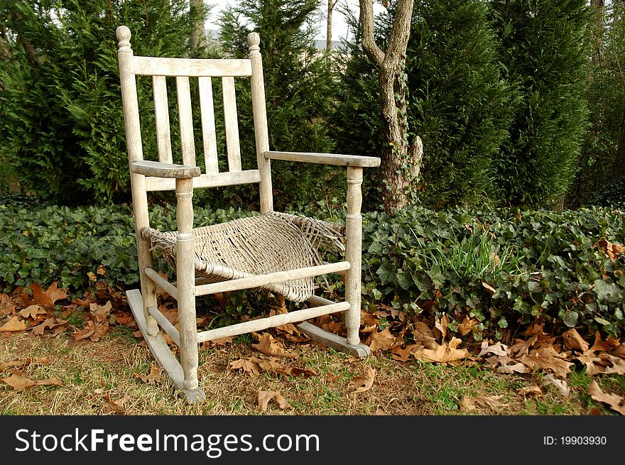 Old weathered rocking chair in yard surrounded by greens, ivy and old leaves. Old weathered rocking chair in yard surrounded by greens, ivy and old leaves